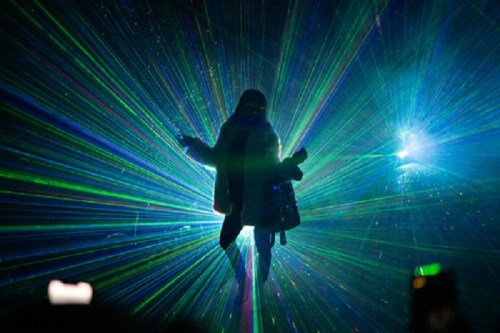 A silhouette of a person dancing amidst vibrant laser lights in a dark setting.