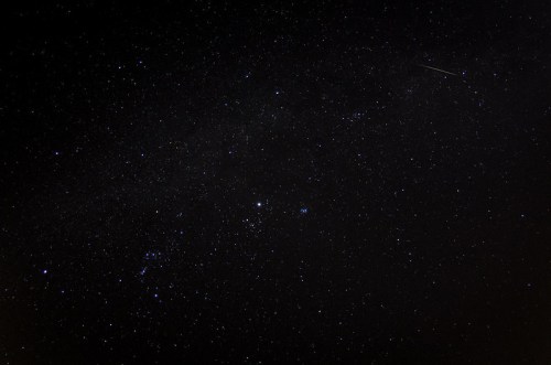 A starry night sky filled with countless stars and a faint streak of a meteor.