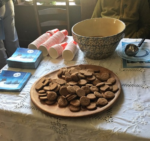 A wooden platter of cookies on a table with cups, a bowl, and coasters in a cozy setting.
