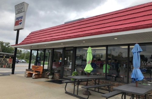 Exterior of a restaurant with a red roof, outdoor seating, and a Pepsi sign, under a cloudy sky.