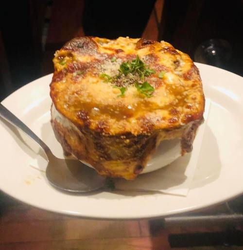 A baked dish with golden, cheesy topping, served in a white bowl on a plate, garnished with herbs.