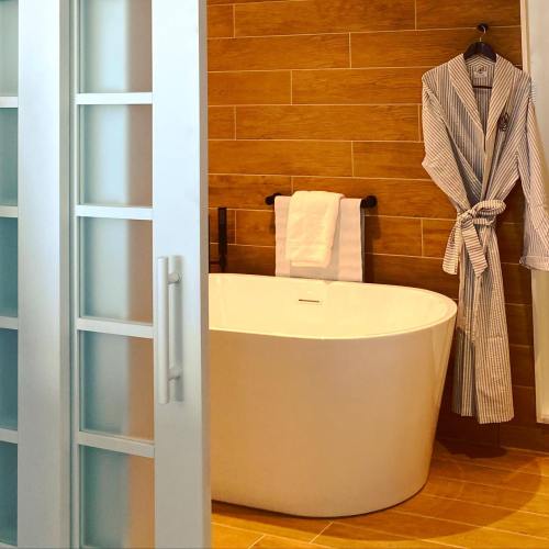 A modern bathroom featuring a freestanding tub, wooden walls, and a striped bathrobe hanging on a towel rack.