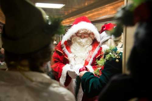 A person dressed as Santa Claus interacts with others in festive attire, surrounded by holiday decorations.