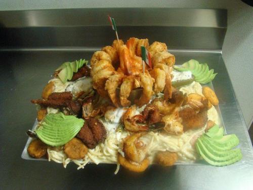 A large seafood platter featuring shrimp, fish, and plantains, garnished with avocado slices and decorative flags.