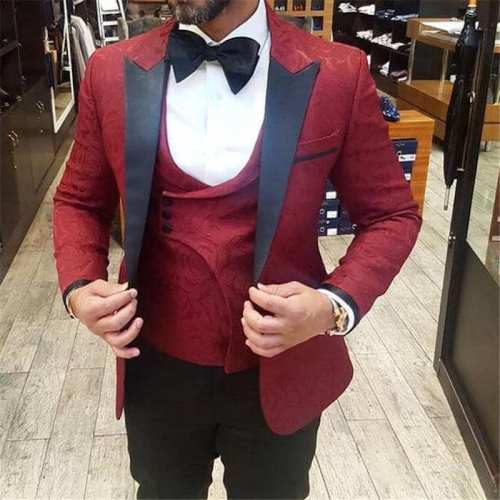 A man in a stylish red tuxedo with a black bow tie, posing confidently in a clothing store.