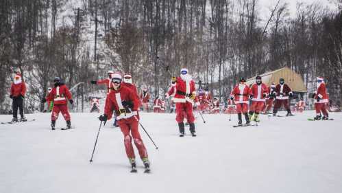 A group of skiers dressed in Santa costumes skiing down a snowy slope. Trees and a building are in the background.