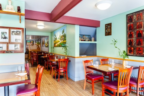 Cozy restaurant interior with wooden tables, chairs, and colorful wall art, creating a warm and inviting atmosphere.