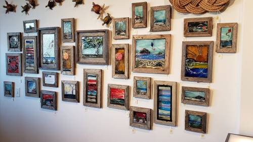 A gallery wall featuring various framed artworks, including landscapes and abstract pieces, in rustic frames.