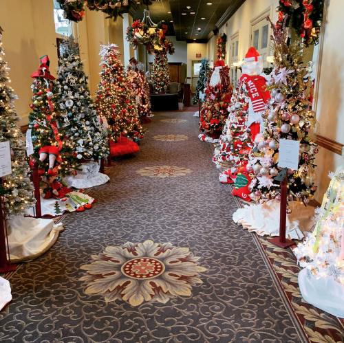 A festive hallway lined with decorated Christmas trees and holiday decorations, creating a cheerful atmosphere.