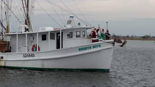 A fishing boat named "Buddy's Boys" on water, with people dressed as Santa waving from the deck.