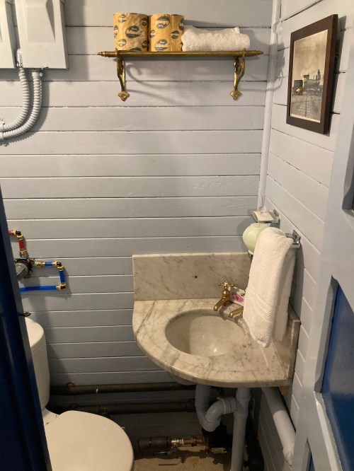 A small bathroom with a marble sink, toilet, shelf with towels, and decorative items on the wall.