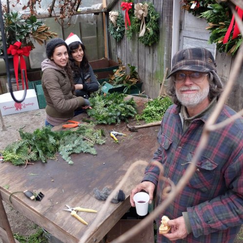 Three people work together at a table, arranging greenery and decorations for the holidays in a festive setting.