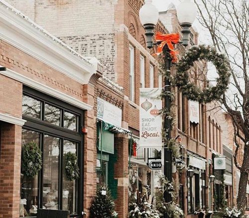A charming winter street scene with brick buildings, festive decorations, and a sign that says "Open."