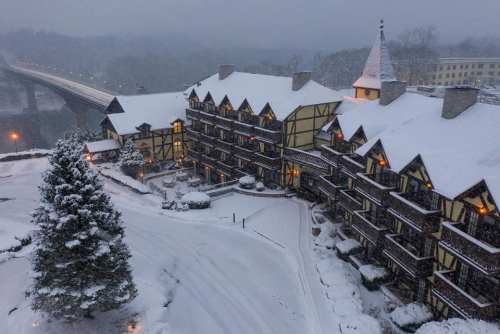 A snowy hotel with a charming architectural style, surrounded by trees and a winter landscape. Soft lights glow from the windows.