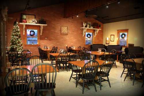 Cozy restaurant interior with wooden tables, black chairs, and festive decorations, including a Christmas tree.