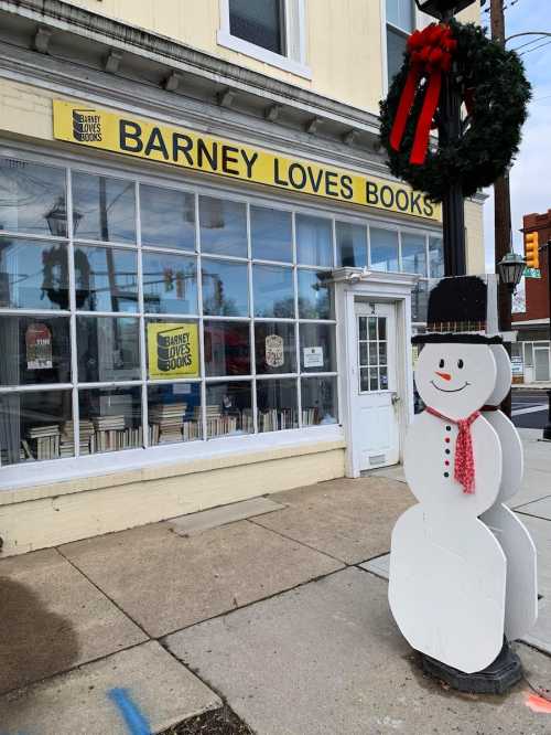 A bookstore named "Barney Loves Books" with a snowman decoration and a festive wreath on the lamp post outside.