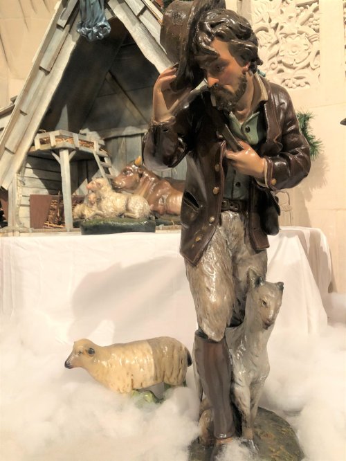 A detailed figurine of a man in a coat, holding a hat, walking with a sheep and a goat in a snowy setting.