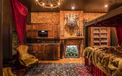 Cozy room with rustic decor, featuring a wooden fireplace, plush seating, and rich red curtains.