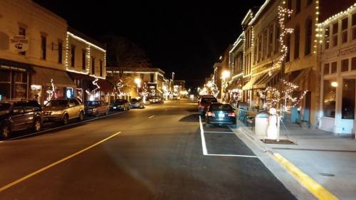 A quiet street at night, lined with buildings adorned with festive lights and parked cars.
