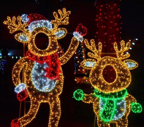 Two illuminated reindeer figures decorated with colorful lights, one wearing a Santa hat and a red scarf, the other in green.