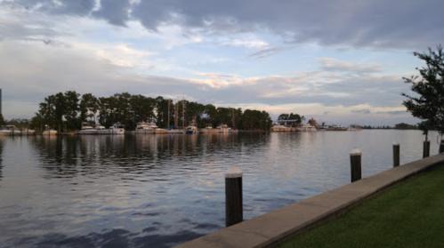 A calm river scene at sunset, with boats docked along the shore and trees lining the water's edge.