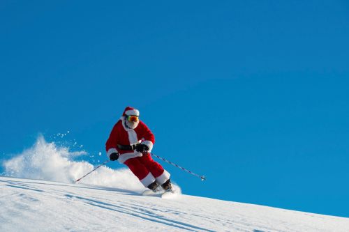 A person dressed as Santa skiing down a snowy slope against a clear blue sky.
