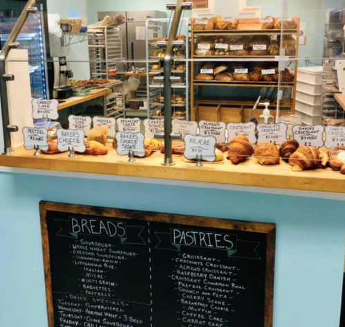 A bakery display with various pastries and breads, featuring a chalkboard menu listing items.