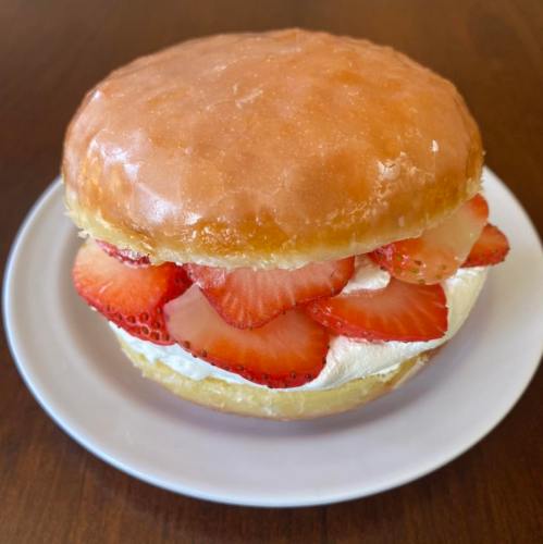 A glazed donut filled with whipped cream and fresh strawberry slices, served on a white plate.