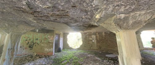 Interior of a dilapidated building with graffiti on the walls and sunlight streaming through broken windows.