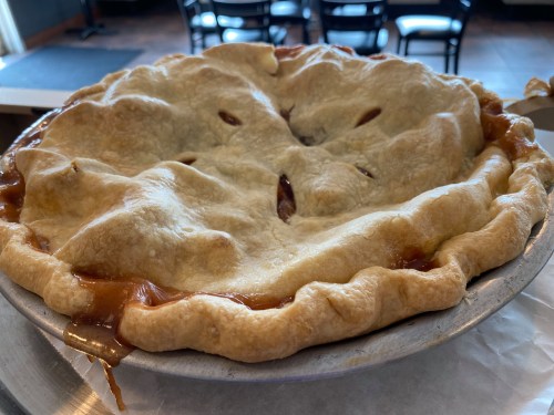 A freshly baked pie with a golden-brown crust, sitting in a metal pie dish, with some filling oozing out.