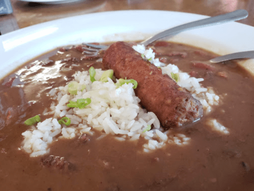 A bowl of brown stew with rice and a sausage, garnished with chopped green onions.