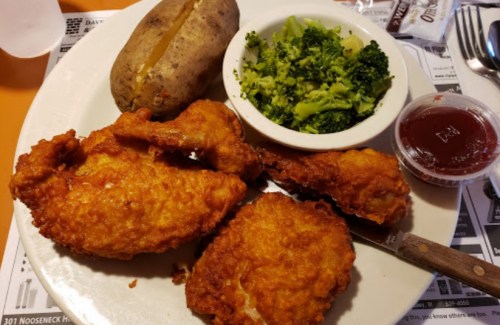 A plate with fried chicken, a baked potato, steamed broccoli, and a small cup of dipping sauce.