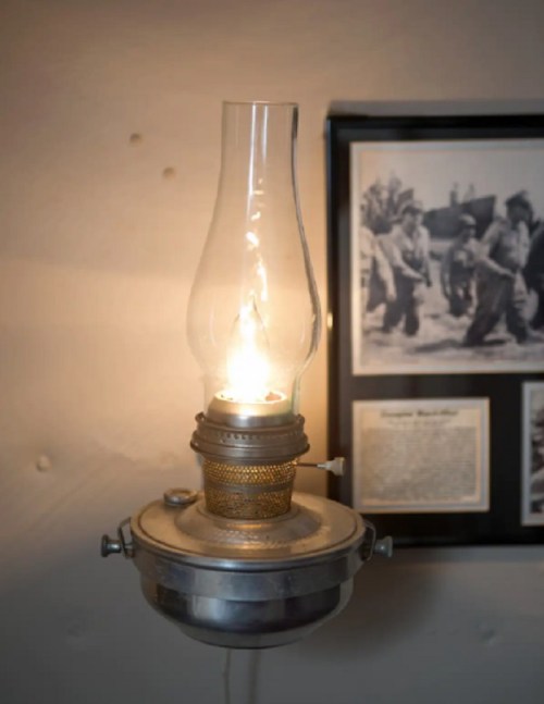 A vintage oil lamp mounted on a wall, glowing warmly, with a historical photo in the background.