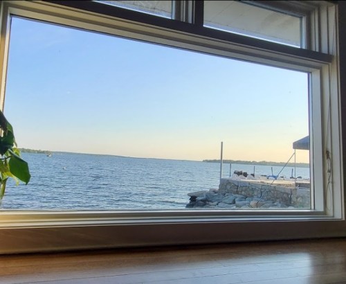 A serene view of a lake through a large window, with a stone dock and a clear sky in the background.