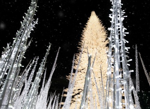 A brightly lit Christmas tree surrounded by glowing white decorations, set against a dark, snowy background.