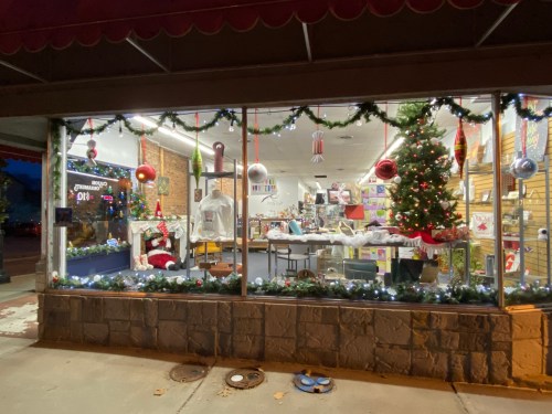 A festive storefront decorated for the holidays, featuring a Christmas tree, ornaments, and seasonal displays.