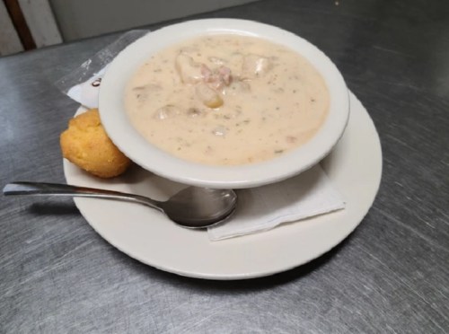 A bowl of creamy soup with chunks of meat and vegetables, served with a cornbread muffin on a plate.