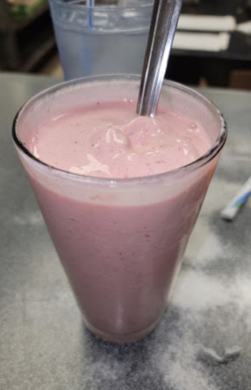 A tall glass filled with a pink smoothie, topped with ice and a spoon resting inside.