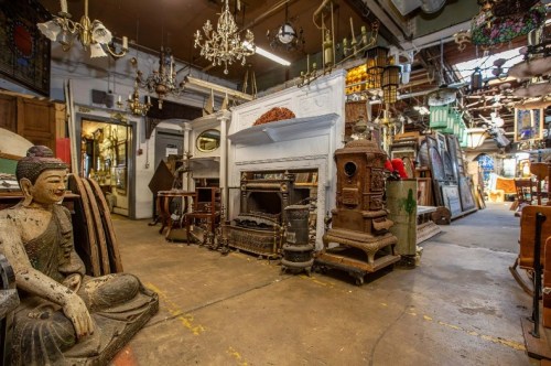 A cluttered antique shop filled with various vintage items, including a statue, furniture, and decorative pieces.