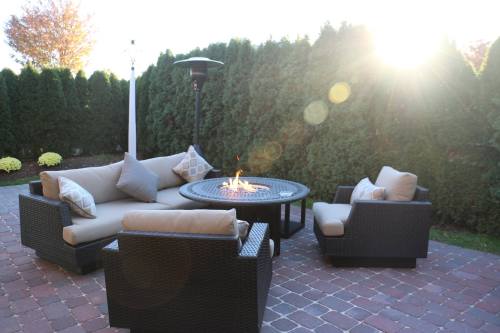 Cozy outdoor seating area with a fire pit, surrounded by greenery and bathed in warm sunlight.
