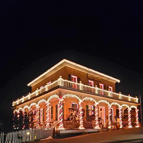 A beautifully decorated house with colorful lights and festive ornaments, set against a dark evening sky.