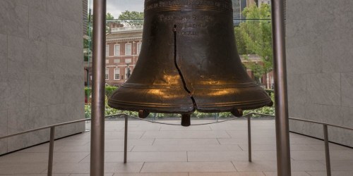 The Liberty Bell displayed in a glass pavilion, showcasing its iconic crack and historic significance.