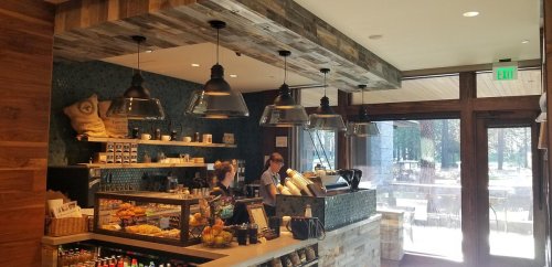 A cozy café interior with wooden decor, a counter displaying pastries, and two baristas preparing drinks.