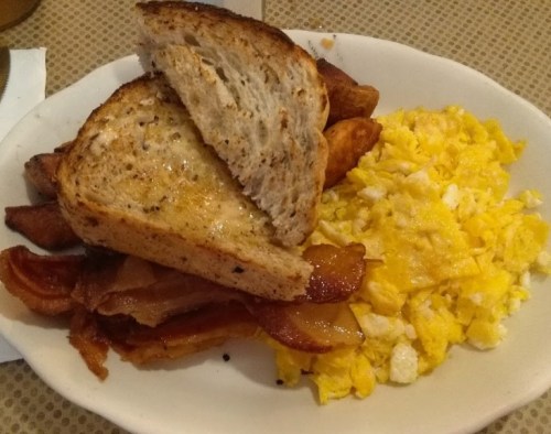 A plate with scrambled eggs, crispy bacon, fried potatoes, and two slices of toasted bread.
