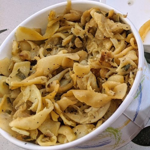 A bowl of cooked noodles mixed with herbs and spices, appearing slightly oily and golden brown.