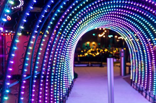 A colorful illuminated archway made of lights, creating a vibrant tunnel effect in a festive setting.