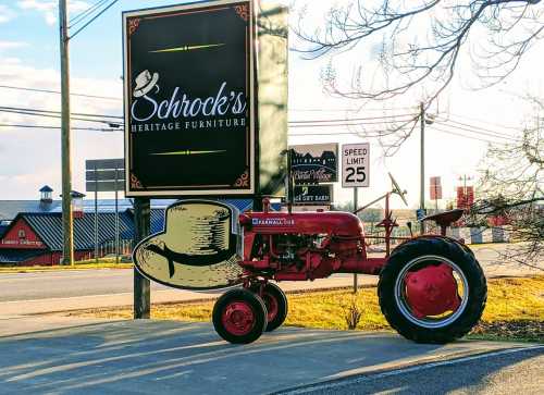 A red vintage tractor parked near a sign for Schrock's Heritage Furniture, with a large hat graphic on the tractor.