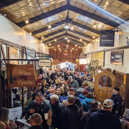 A bustling indoor market filled with people browsing various stalls under a high, lit ceiling.