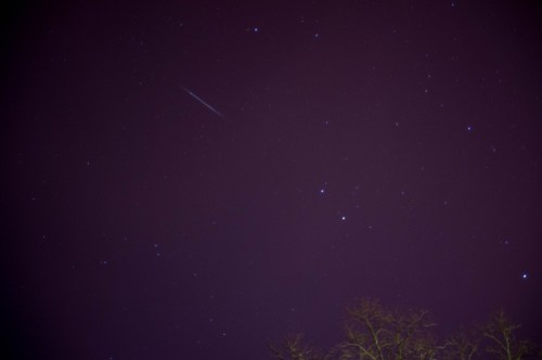 A night sky filled with stars, featuring a faint meteor streaking across the dark background.