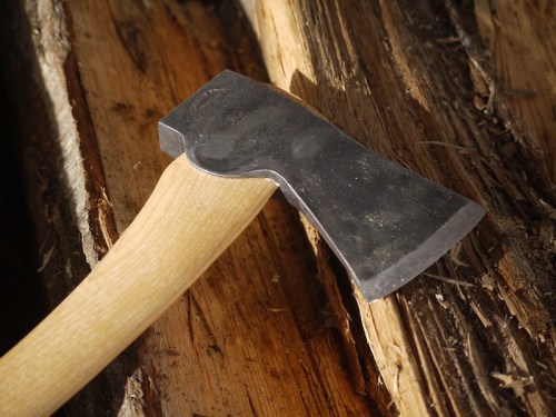Close-up of a metal axe head resting on a wooden surface, showcasing its sharp edge and smooth wooden handle.